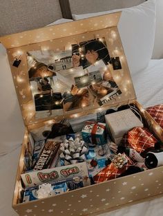 an open box filled with personal items on top of a white bed covered in lights