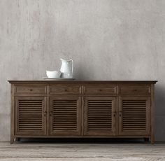 a wooden sideboard with shutter doors on the bottom and two white dishes on top