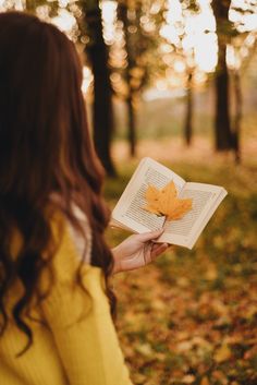 a woman is holding an open book in the park with autumn leaves on her hands