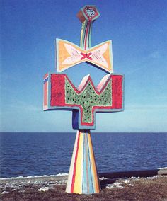 a colorful sculpture on the beach with water in the backgrounnd and blue sky