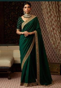 a woman wearing a green sari with gold detailing on the neck and shoulder, standing in