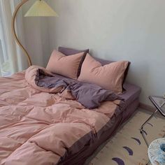 an unmade bed with pink sheets and pillows in a room next to a window