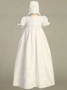 Details Timeless Baptism or Christening gown is made of a soft pure white cotton. Short puffed cap sleeves w/ lace trim. Smocked embroidered detail on bodice. Skirt has plain cotton pleats along with a ribbon lace detail towards the bottom of the skirt as well as at the bottom edge. Irremovable tie back sash. Three pearl colored button back closure. Matching bonnet included that includes a ribbon lace detail, a ruffled edge and a long satin ribbon tie. Sizes Available: X-Small (0-3 Months), Smal Elegant Fitted Baptism Dress With Smocked Bodice, White Baptism Dress With Smocked Bodice For First Communion, Elegant Baptism Dress With Smocked Bodice, Classic Short Sleeve Baptism Dress With Ruffles, White Fitted Baptism Dress With Smocked Back, Classic Baptism Dress With Ruffles, Classic First Communion Dress With Lace Trim, Classic Short Sleeve Cotton Baptism Dress, Baptism Gown