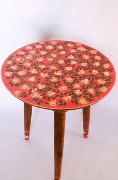 a red table with gold and green designs on the top sits against a white background