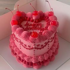 a pink heart shaped cake with cherries on top in a white card board box