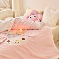 a pink bed with two pillows and a teddy bear on it, next to a lit candle