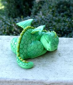 a green dragon figurine sitting on top of a cement wall next to bushes