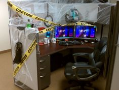 an office cubicle with caution tape on the wall and computer desk in front of it