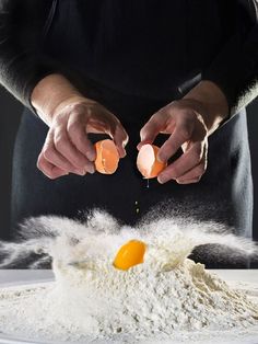 an egg being boiled into flour on top of a white plate with two hands reaching for it