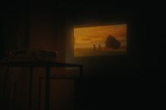 a dark room with a painting on the wall and people walking in the distance at night