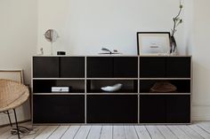 a room with white walls and wooden flooring has a black bookcase on the side