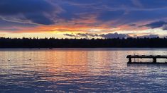 a dock in the middle of a body of water at sunset with clouds above it