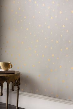 a table with a cup on it next to a wall that has gold stars painted on it