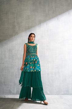 Enhance the elegance of yourself with this stylish and comfortable gharara set, a three piece ensemble, ensuring a stunning appearance on any occasion. Crafted from premium-quality georgette fabric in a green hue, this ensemble comprises a top, bottom, and dupatta. The peplum style top is a masterpiece of meticulous artistry, adorned with intricate floral prints and sequin work in the yoke portion subtly highlighted by the shimmer of mirrors, which adds a touch of refinement throughout. Tassels around the waistline add beauty. The gharara-style bottom, with its fine pleats and secure hook closure, imparts a voluminous and graceful appearance in two tiers. The dupatta, in the same matching hue, is adorned with lace detailing throughout, elevating the overall elegance of the ensemble. Note: Green Floor-length Designer Wear Sets, Green Straight Kurta Palazzo Set With Sheer Dupatta, Designer Green Palazzo Set For Festive Occasions, Green Designer Palazzo Set For Diwali, Green Palazzo Set For Diwali Designer Wear, Semi-stitched Green Bollywood Palazzo Set, Green Anarkali Palazzo Set With Sheer Dupatta, Fitted Green Georgette Palazzo Set, Bollywood Style Green Semi-stitched Palazzo Set