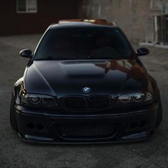 the front end of a black car parked in a parking lot next to a building