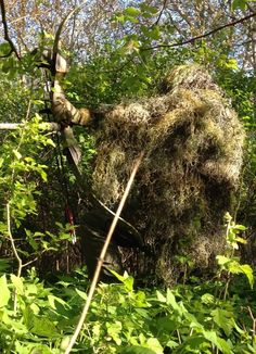 a man in the woods with a large bushel on his back and arms extended out