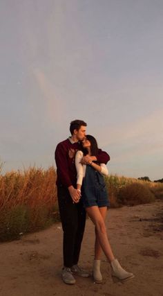 a man and woman standing next to each other on a dirt road with tall grass in the background