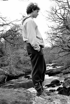 a young man standing on top of a rock next to a river with trees in the background