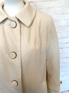 "60s Susan Lynn textured fabric lightweight coat. Coat is in a winter white Large tarnished brass/copper colored buttons covered in coat fabric. Strap with button on both cuffs and on the back. 2 side pockets Fully lined and no stains or tears Excellent vintage condition No fabric or size tag. Most likely a polyester blend and a size large, go by the measurements. Measurements when laying flat across: Bust - 21\" Sleeve - 21\" Length - 30\"" Cream Collared Outerwear With Button Cuffs, Classic Cream Outerwear With Button Cuffs, Beige Collared Blazer With Buttons, Vintage Solid Blazer With Button Closure, Cream Outerwear With Lapel Collar And Buttons, Spring Cream Outerwear With Covered Buttons, Cream Pea Coat With Button Closure For Spring, Spring Solid Outerwear With Covered Buttons, Spring Outerwear With Covered Buttons