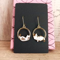 Cute golden hoop earrings with mismatched cats. One cat rests facing forward and the other one on its back.  Lovely valentines day gift for cat lovers Hypoallergenic stainless steel hooks. Enameled alloy metal rings with cats.  Hoops diameter is 2.2cms  Total drop length is 4.5cms  Weight: 2.6g These earrings are carefully shipped in a cardboard box to guarantee you will receive them in perfect conditions. Please specify if you want them as a gift when you are ordering. No additional cost Cardboardbox is handmade with recycled and sustainable material. #hoopearrings #cathoopearrings #carearrings #catlover #originalgift #originalhoops #originalearrings #catjewelry #cataccesories #mismatchedcatearrings #mismatchedearrings #valentinesday #giftforvalentinesday #loversday #friendshippresent #fr Metal Jewelry With Cat Design, Metal Cat Design Round Jewelry, Gold Cat Ears Jewelry Gift, Gold Cat Ears Jewelry As Gift, Gold Cat Ears Jewelry For Gifts, Gold Cat Design Earrings For Gifts, Gold Cat Ears Jewelry For Gift, Cat Design Metal Drop Earrings, Gold Metal Cat Design Earrings