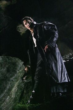 a man in a trench coat is standing on some rocks