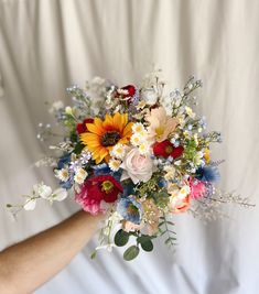 a person holding a bouquet of flowers on a white sheet with their hand in the air