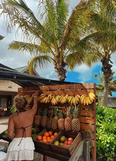 a woman standing next to a fruit stand with bananas and pineapples on it