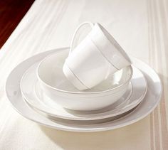 a stack of white plates and cups sitting on top of a tablecloth covered table