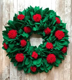 a green wreath with red flowers hanging on a wooden wall in front of a white fence