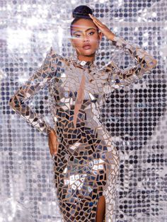 a woman standing in front of a silver background wearing a dress with sequins on it