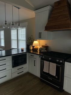 a kitchen with white cabinets and black counter tops is lit by two pendant lights above the stove