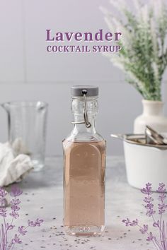 a bottle of lavender cocktail syrup sitting on top of a table next to some flowers