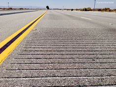 an empty road with yellow lines on the side and blue sky in the back ground