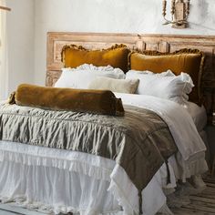 a bed with white sheets and gold pillows on it's headboard, next to a window