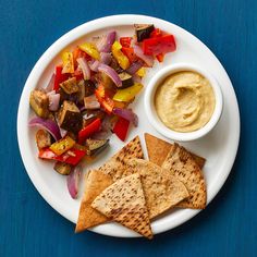 a white plate topped with pita bread and veggies next to a bowl of hummus