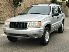 a silver jeep parked in a parking lot next to a wall with trees on it