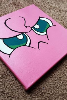 a pink square with eyes painted on it sitting on the floor in front of a carpeted area