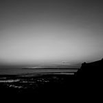 a black and white photo of the ocean at sunset