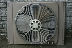 an old air conditioner fan sitting on the side of a brick wall in front of a building