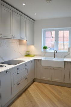 a kitchen with white cabinets and wood floors is pictured in this image, there is a window over the sink