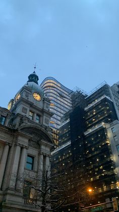 an old building with a clock on the top in front of other tall buildings at dusk