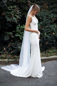 a woman in a white wedding dress standing on the street wearing a veil over her head