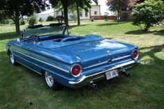 an old blue convertible car parked in the grass