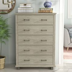 a white dresser sitting in a living room next to a mirror and potted plant