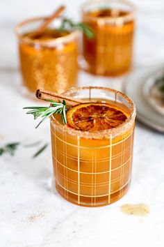 two glasses filled with orange and rosemary garnish sitting on a white tablecloth