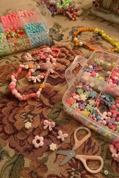 some beads and scissors are laying on the floor next to each other in plastic containers