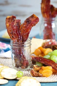 some bacon sticks are in a jar with grapes and crackers on the table next to them