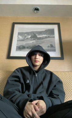 a young man sitting on top of a couch wearing a black hoodie and sweatpants