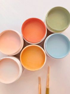 five different colored bowls with paint brushes in them