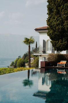 an outdoor swimming pool with lounge chairs and palm trees next to it, overlooking the ocean